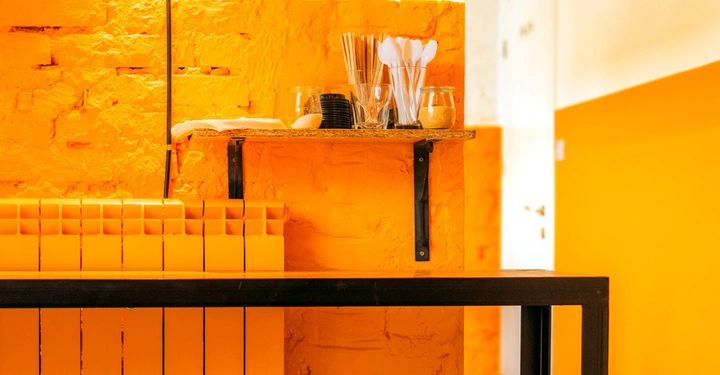 Regal enthält orangefarbene Behälter darauf stehende Gläser und Löffel Holzregal an bunter Wand in gelbem Raum.