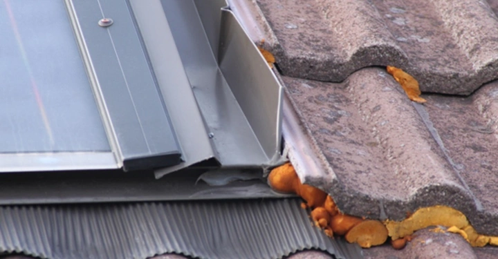 Galerie-Bild 1: Solarmodul liegt teilweise auf braunen Dachziegeln, umgeben von gelblichem Montageschaum, im Freien.