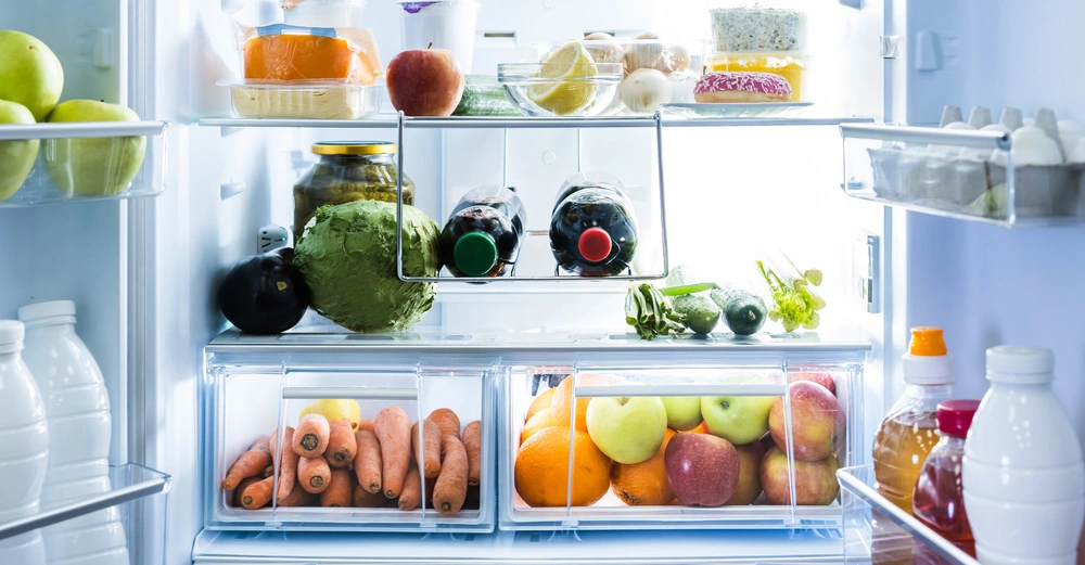 Lebensmittel liegen im Kühlschrank sortiert Optionen sind Käse Apfel Karotten Salat Kopfsalat Gurken Zitrone Saucen Plastikflaschen und Glasgefäße in den Regalen in einem gut beleuchteten, sauberen Innenraum.