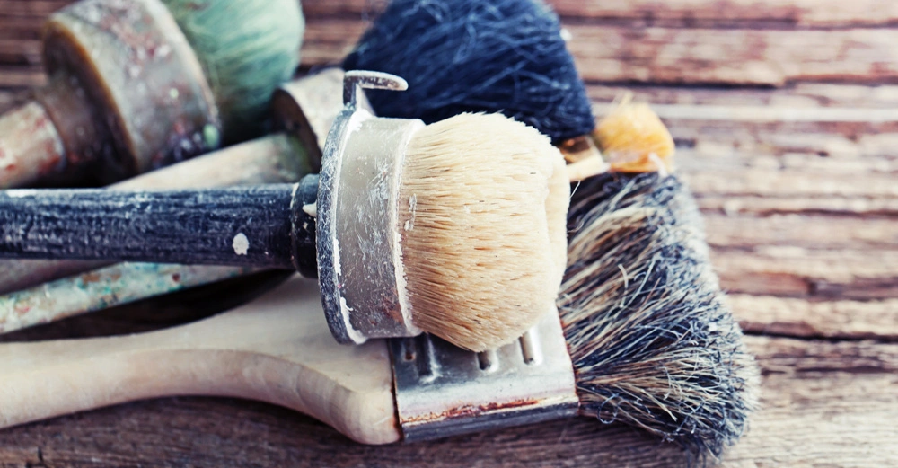 Verschiedene abgenutzte Pinsel liegen zusammen verworren auf einem rustikalen Holztisch.