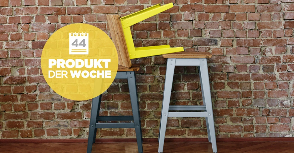 Hocker stehen auf einem Holzboden vor einer Backsteinmauer ein Hocker liegt umgedreht auf einem anderen Hocker Gelber Kreis zeigt Text 44 PRODUKT DER WOCHE