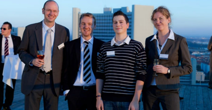 Galerie-Bild 9: Mehrere Personen stehen lächelnd auf einer Dachterrasse Hochhaus im Hintergrund zwei Personen halten Getränke in den Händen formelle Kleidung einige Personen im hinteren Bereich societal environment