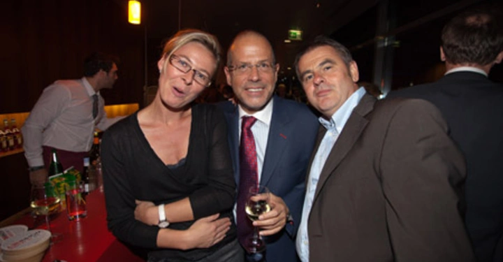 Galerie-Bild 84: Drei Personen posieren lächelnd für ein Foto Dreier ist bei einem gesellschaftlichen Event in einem modernen Innenraum In der Nähe stehen Getränke und Gläser auf einer Bar.