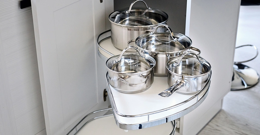 Moderner Eckschrank in einer weißen Küche mit glänzenden Töpfen auf ausziehbaren Ablagen.