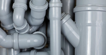 Graue PVC-Rohre sind ineinander verschlungen angeordnet in einer Nahaufnahme innerhalb eines Rohrleitungssystems. Die Rohre zeigen verschiedene Biegungen und Verzweigungen, bilden ein komplexes Netzwerk.