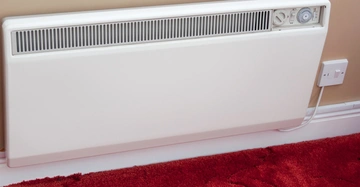 Ein weißer Heizkörper hängt an einer beigen Wand und ist an eine Steckdose angeschlossen Ein roter Teppich bedeckt den Boden darunter.