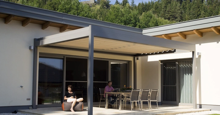 Galerie-Bild 4: Eine Frau sitzt und liest auf einem Sitzsack eine Person sitzt am Tisch auf einer Terrasse im modernen Garten einer Wohnung umgeben von Wald und Hügeln mit einer Burg im Hintergrund