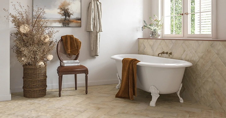 freistehende weiße Badewanne mit Füßchen steht vor Badezimmerfenster, ein rotes Handtuch hängt über den Wannenrand. Links im Bild ein Holzstuhl und eine große Pflanze. 