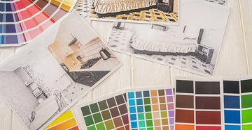 Tischplatte eines Planers, auf der verschiedene Farbpaletten und Fotos von Wohnräumen verstreut liegen.
