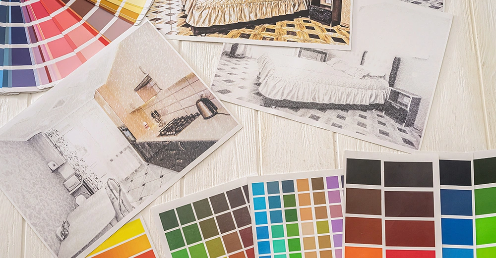 Tischplatte eines Planers, auf der verschiedene Farbpaletten und Fotos von Wohnräumen verstreut liegen.