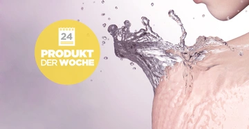 Wasser spritzt auf eine nackte Schulter in einem minimalistisch gestalteten Raum linkerseits befindet sich ein gelber Kreis mit der weißen Aufschrift 24 Produkt der Woche