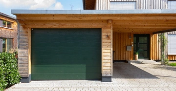 Grünes Garagentor geschlossen Holzhäuser im modernen Stil umgeben von gepflastertem Boden und Pflanzen. Houdartige Verkleidung Fensterläden geschlossen helle Tageslichtbeleuchtung.