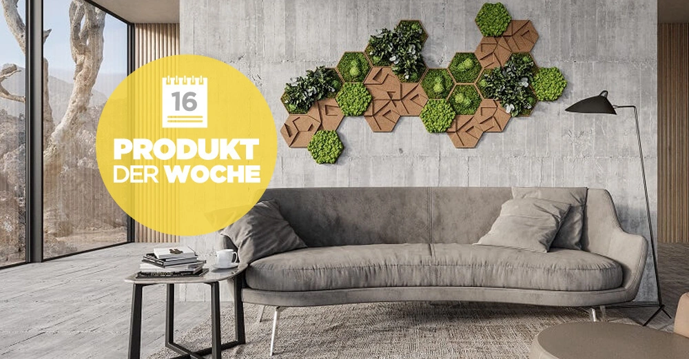Graues Sofa steht vor einer Betonwand mit hexagonalen Pflanzenbildern dekoriert in modernem Wohnzimmer mit großen Fenstern. Text auf gelbem Kreis 16 PRODUKT DER WOCHE.