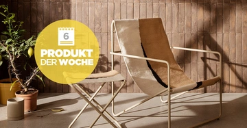 Ein beiger Stuhl steht neben einem Hocker auf einem Betonboden mit einem Pflanzentopf dahinter vor einer holzverkleideten Wand. Text: 6 PRODUKT DER WOCHE