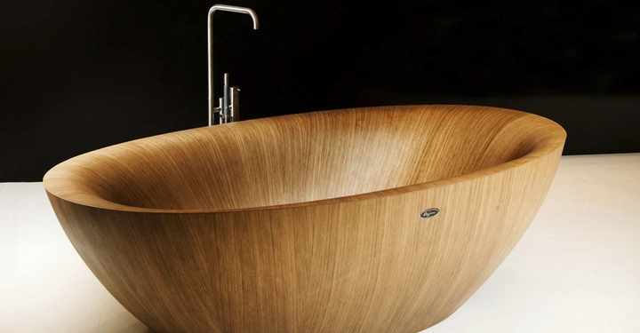 Eine freistehende hölzerne Badewanne steht auf einem weißen Boden vor einer schwarzen Wand ein moderner Wasserhahn ist dahinter angebracht