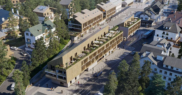 Luftaufnahme eines großen Hotels aus Holz mit vorgelagerten Terrassen und länglichem Baukörper.