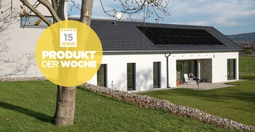 Baum steht still auf grünem Rasen vor modernem weißem Haus mit großen Fenstern und Solarpanelen auf dem Dach in ländlicher Umgebung Text: 15 Produkt der Woche