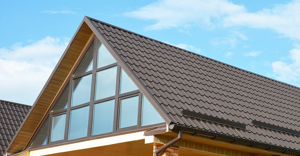 Giebel eines Backsteinhauses mit großen Fenstern und einem dunkel gedeckten Satteldach unter einem blauen Himmel mit vereinzelten Wolken