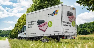 Kleinlastwagen von Austrotherm steht auf Baustelle. Mehrere Säcke mit Dämmresten stehen vor der Ladefläche.