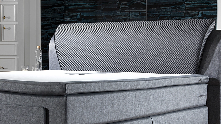 Boxspringbett mit grauem Stoffbezug und hoher Boxspringmatratze plus weißem Topper