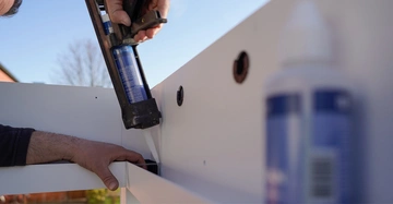 Mann verfüllt mit einer Silikonpistole eine Fuge an einer Überdachung