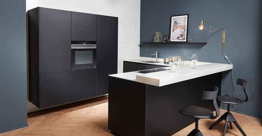 Schwarze Küchenschränke integriert ein Ofen nimmt Hauptbereich ein Moderne Küchengeräte und Dekorationsgegenstände auf der Arbeitsplatte und einem Regal in einem stilvollen Kücheninnenraum mit Holzboden und blauen Wänden