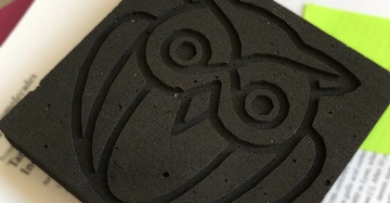 Schwarzer Schaumstoffblock zeigt das eingeprägte Bild einer Eule sitzt auf einer Unterlage bestehend aus verdecktem Text auf Papier und einem gelben Leuchtstiftpapier im Hintergrund.