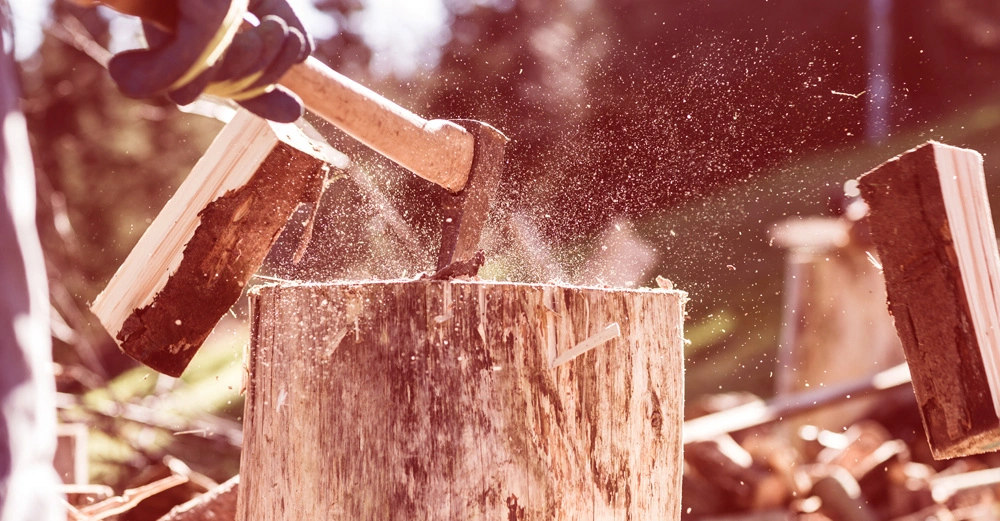 Eine Axt schlägt Holz auf einem Baumstumpf Rücken eines Gärtners in Handschuhen Bäume und Holzstapel im Hintergrund in einer Waldlandschaft