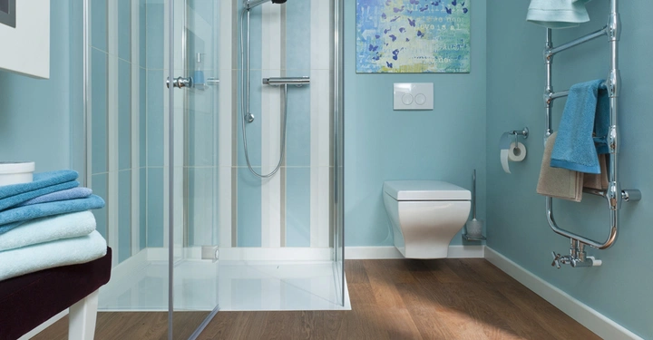 Galerie-Bild 7: Ein modernes Badezimmer zeigt eine offene Duschkabine neben einem Wand-WC. Im Raum hängen Handtücher auf einem silbernen Handtuchhalter, und auf dem Boden liegen Handtücher gestapelt.