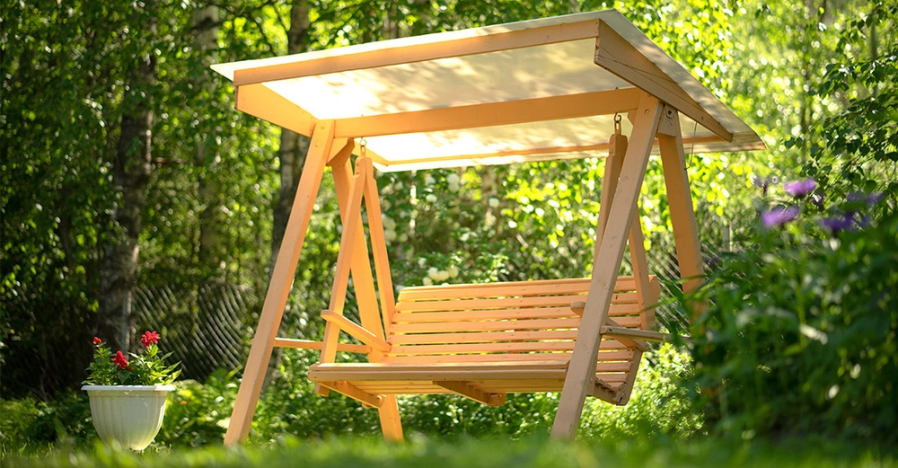 Hölzerne Hollywoodschaukel vom Licht beschienen im grünen Garten.