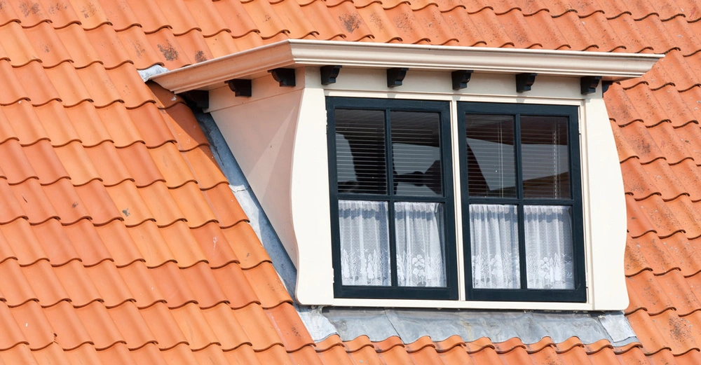 Ein Dach, das mit roten Ziegeln gedeckt ist und aus dem eine weiße Dachgaube hervorsteht.