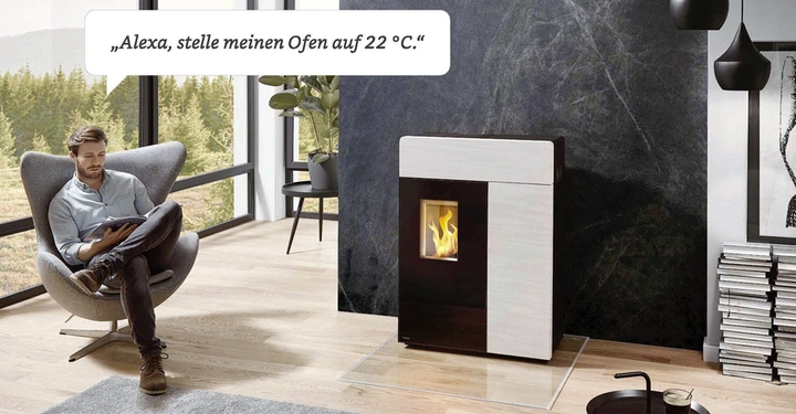 Ein Mann sitzt in einem Stuhl und liest auf einem Tablet in einem modernen Wohnzimmer neben einem Ofen. Text: Alexa stelle meinen Ofen auf 22 °C