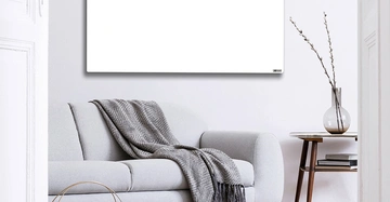 Graues Sofa liegend darauf eine gefaltete Decke in einem Wohnzimmer daneben ein kleiner Holz-Tisch mit Glasvase Weiße Wand Vordergrund geöffnete weiße Tür oben rechteckiger weißer leerer Rahmen