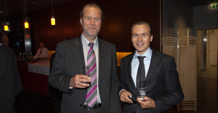 Galerie-Bild 80: Zwei Männer in Anzügen stehen nebeneinander und halten Getränke in einem Raum mit gedämpfter Beleuchtung Bar im Hintergrund Barmann im Hintergrund Vorhänge und Räume sichtbar rechts