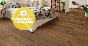 Bett mit gemusterten Bettdecken steht auf Holzboden in einem modern eingerichteten Schlafzimmer mit Pflanzen Regalen und großem runden gelben Emblem mit der Aufschrift 31 PRODUKT DER WOCHE