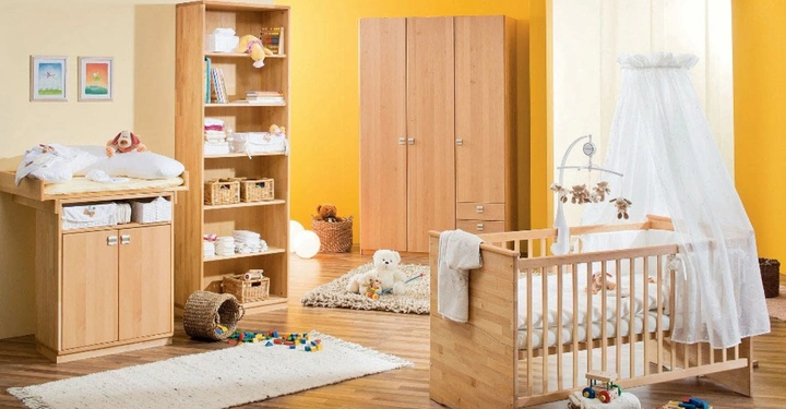 Galerie-Bild 4: Babybett mit Baldachin steht in hellem Kinderzimmer mit Wickeltisch, Regal und Kleiderschrank, während Spielzeug und Bücher das Zimmer schmücken. An der Wand hängen zwei gerahmte Bilder.