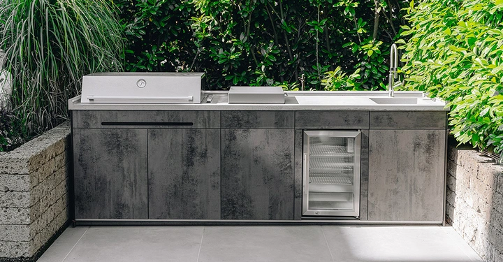 Galerie-Bild 6: Outdoorküche aus HPL mit Betonarbeitsplatte steht vor grüner Hecke im Garten.