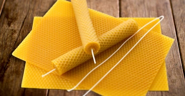 Gelbe gewachste Bienenwaben mit Docht werden gerollt auf einem Holztisch platziert.