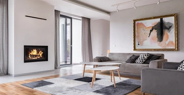 Kamin brennt Wohnzimmer moderne Einrichtung graue Sofas schwarz-weiße Kissen abstraktes Gemälde an der Wand grauer Teppich Holzfußboden große Fenster mit Vorhängen Couchtisch.