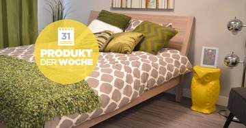 Holzbett mit gemustertem Bettzeug dekoriert mit grünen Kissen und Decke steht in einem modern eingerichteten Schlafzimmer neben gelber Eulen-Dekoration und einer Stehlampe. Text: 31 PRODUKT DER WOCHE.