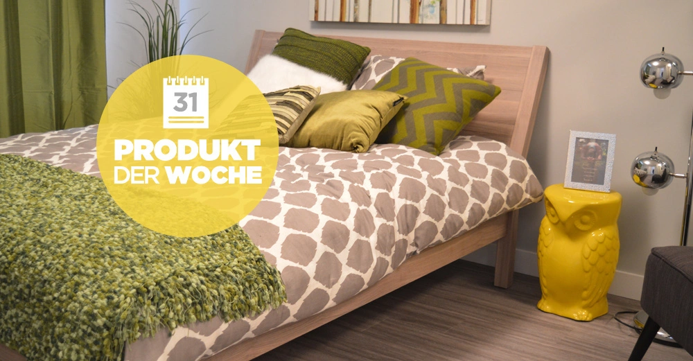 Holzbett mit gemustertem Bettzeug dekoriert mit grünen Kissen und Decke steht in einem modern eingerichteten Schlafzimmer neben gelber Eulen-Dekoration und einer Stehlampe. Text: 31 PRODUKT DER WOCHE.