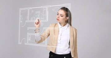 Frau verwendet digitalen Touchscreen zum Erstellen eines Gebäudegrundrisses beige Jacke und weißes Hemd grauer Hintergrund