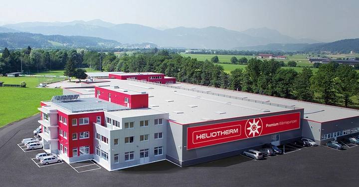 Außenaufnahme vom Firmengebäude von Heliotherm. Modernes Gebäude, umgeben von grüner Landschaft und Bergen. Ideal für umweltfreundliche Heizlösungen.