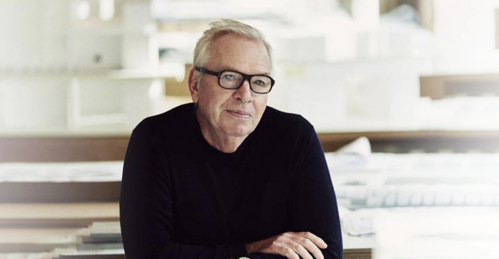 Mann mit Brille lehnt sich nach vorne und schaut nachdenklich im gut beleuchteten Büro voller Papierstapel und Regale