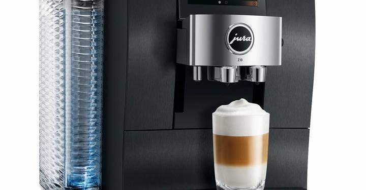 Ein Kaffeevollautomat bereitet einen Latte Macchiato zu. Der Automat steht in einem modernen Küchenumfeld. Auf dem Display des Automaten sind verschiedene Kaffeespezialitäten abgebildet. Text: Jura Z10.