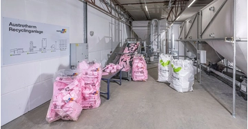 große Säcke mit Dämmstoffabfällen (rosa und weiß) stehen in großer Recyclinganlage.