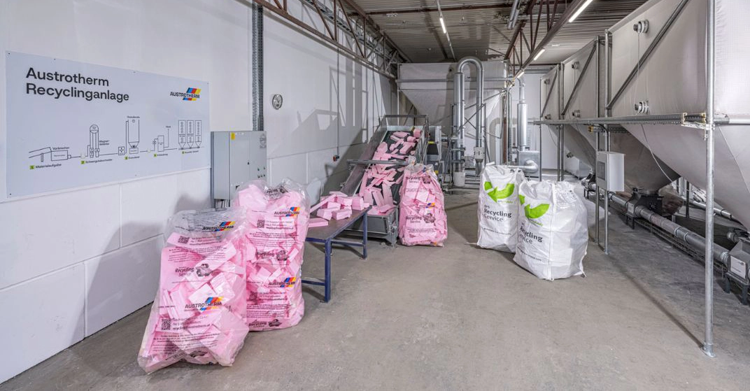 große Säcke mit Dämmstoffabfällen (rosa und weiß) stehen in großer Recyclinganlage.