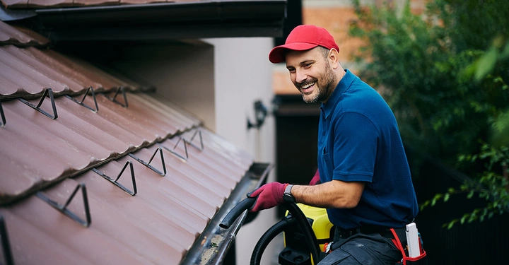 Freundlicher Experte zum Thema Dachentwässerung, reinigt eine Dachrinne mit einem Laubsauger.
