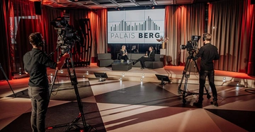 Bühne im Palais Berg in Wien, in dunklem Rot mit zwei elegant gekleideten Frauen, die sich mit Mikrofonen gegenübersietzen. Im Vordergrund Kameraleute und Aufnahmeleiter.