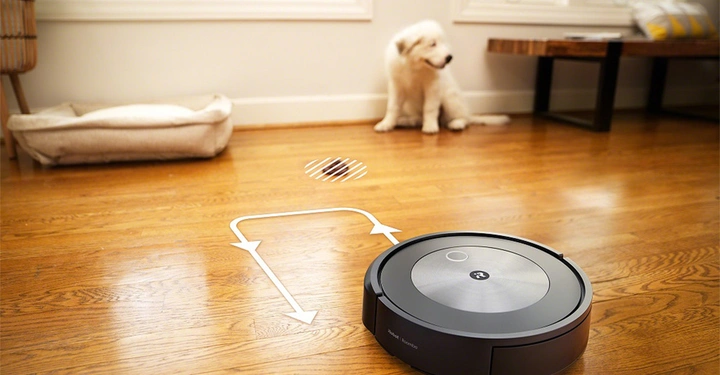 Staubsaugerroboter fährt auf Holzboden Wohnzimmer Hund sitzt vor Hundebett Fenster und Beistelltisch im Hintergrund